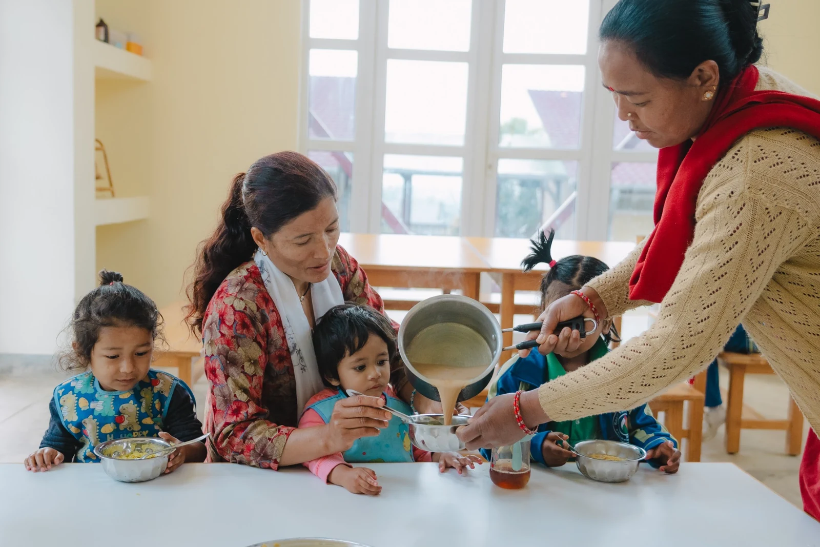 Adults serving a meal to young children seated together at a table.