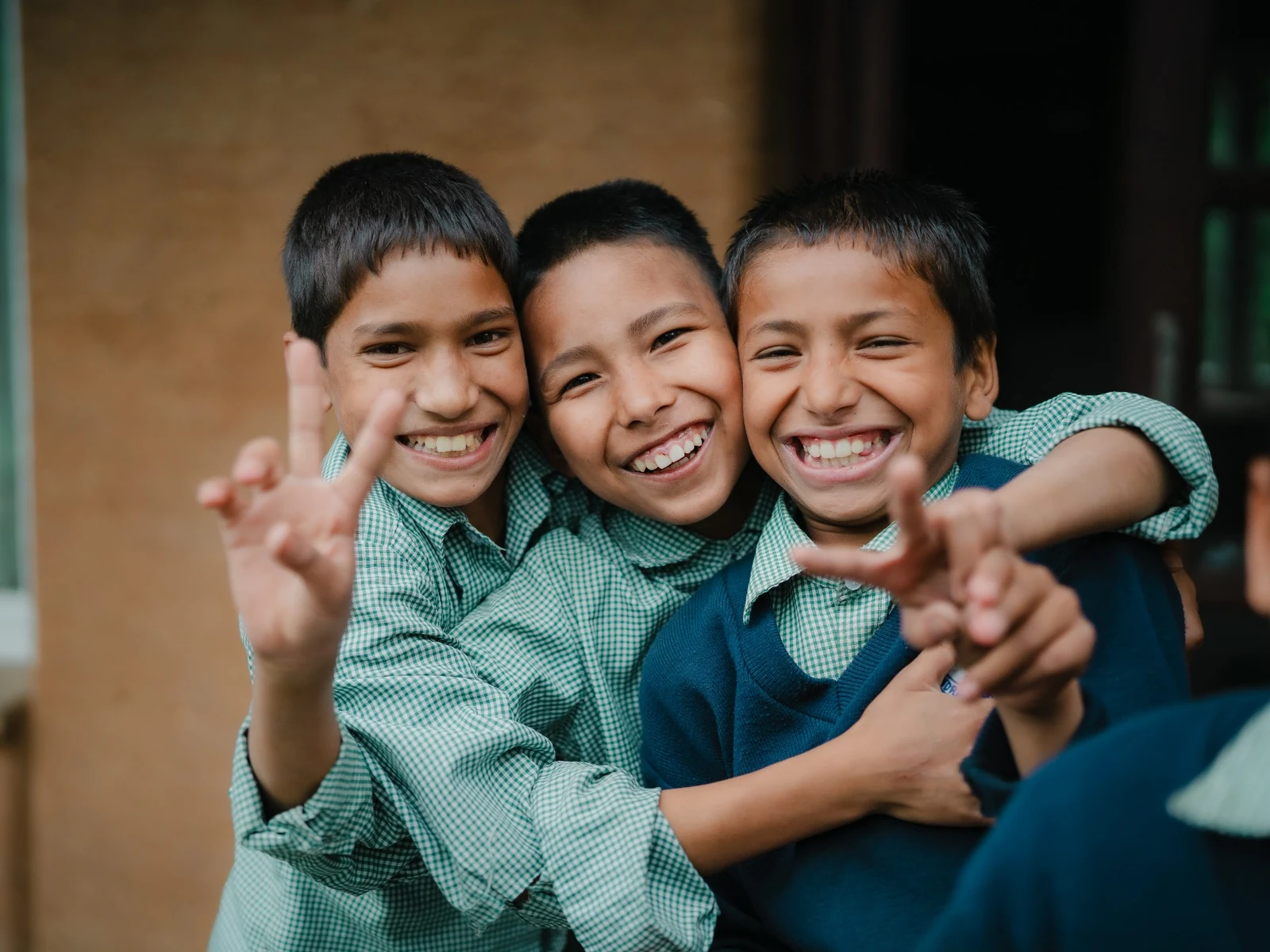 Three smiling children in school uniforms with their arms around one another.